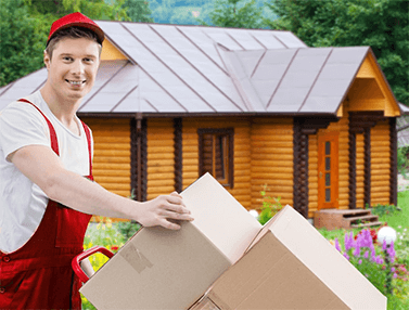 Грузчик улыбается с картонным ящиком в руках на фоне деревянного дома